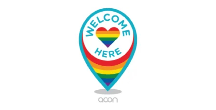 The Welcome Here logo; a location pin shape with a strong aqua coloured outline, with the words “Welcome here” inside, surrounding a rainbow coloured heart.