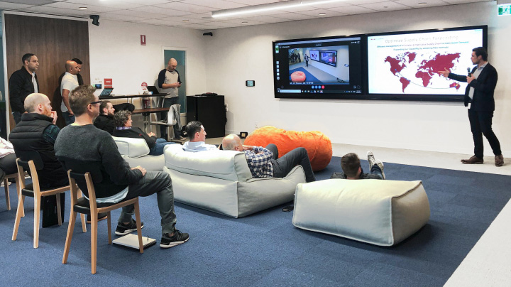 Toyota employees in a lounge with two large TV screens and comfy couches,  intently watching a presentation.