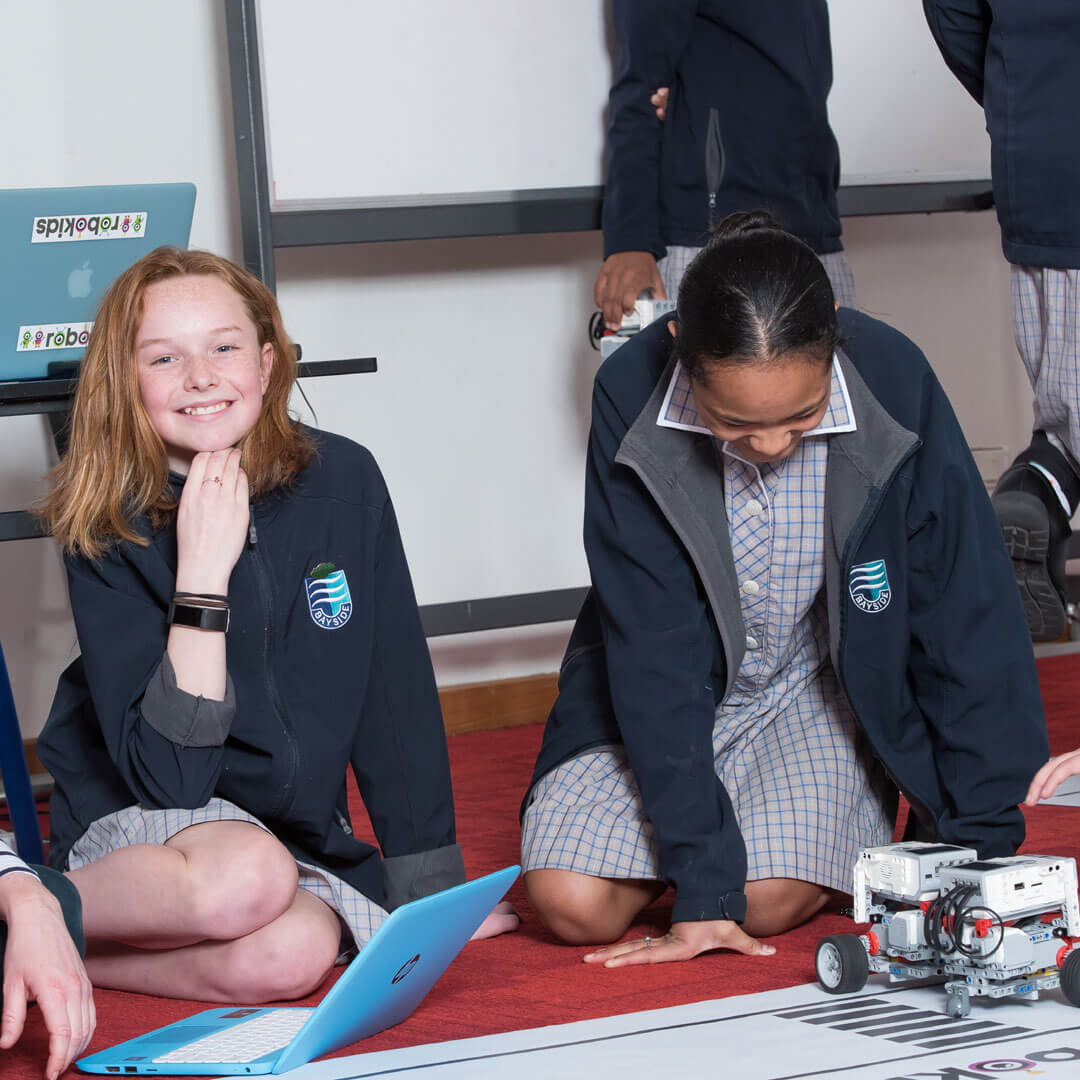 Two uniformed school girls, sitting on the floor participating in Toyota’s STEM workshops. 
