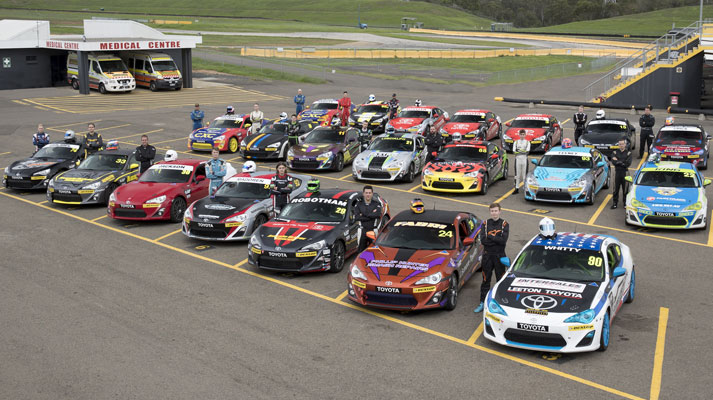 Two rows of Toyota racing vehicles lined up on a racetrack, each with an accompanying race car driver standing proudly next to it.