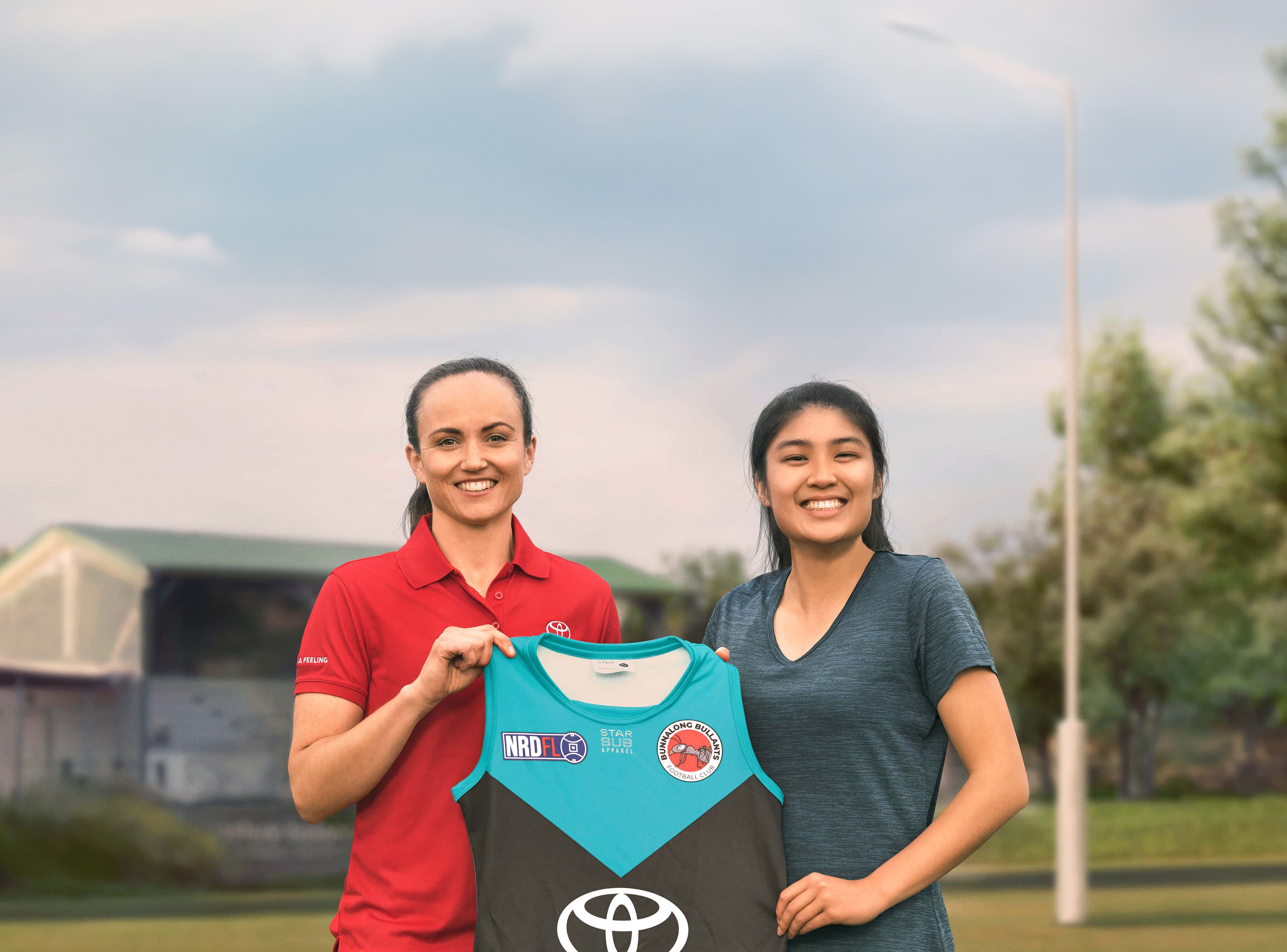Two AFLW players proudly holding up a specially designed womens footy jersey.