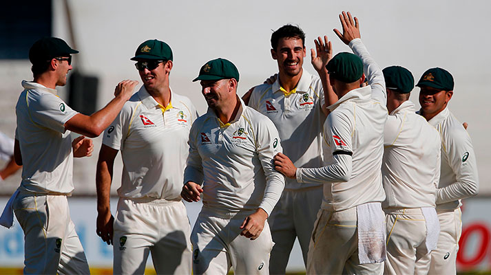 The Australian cricket team high-fiving and celebrating a victory on the pitch on a sunny day.