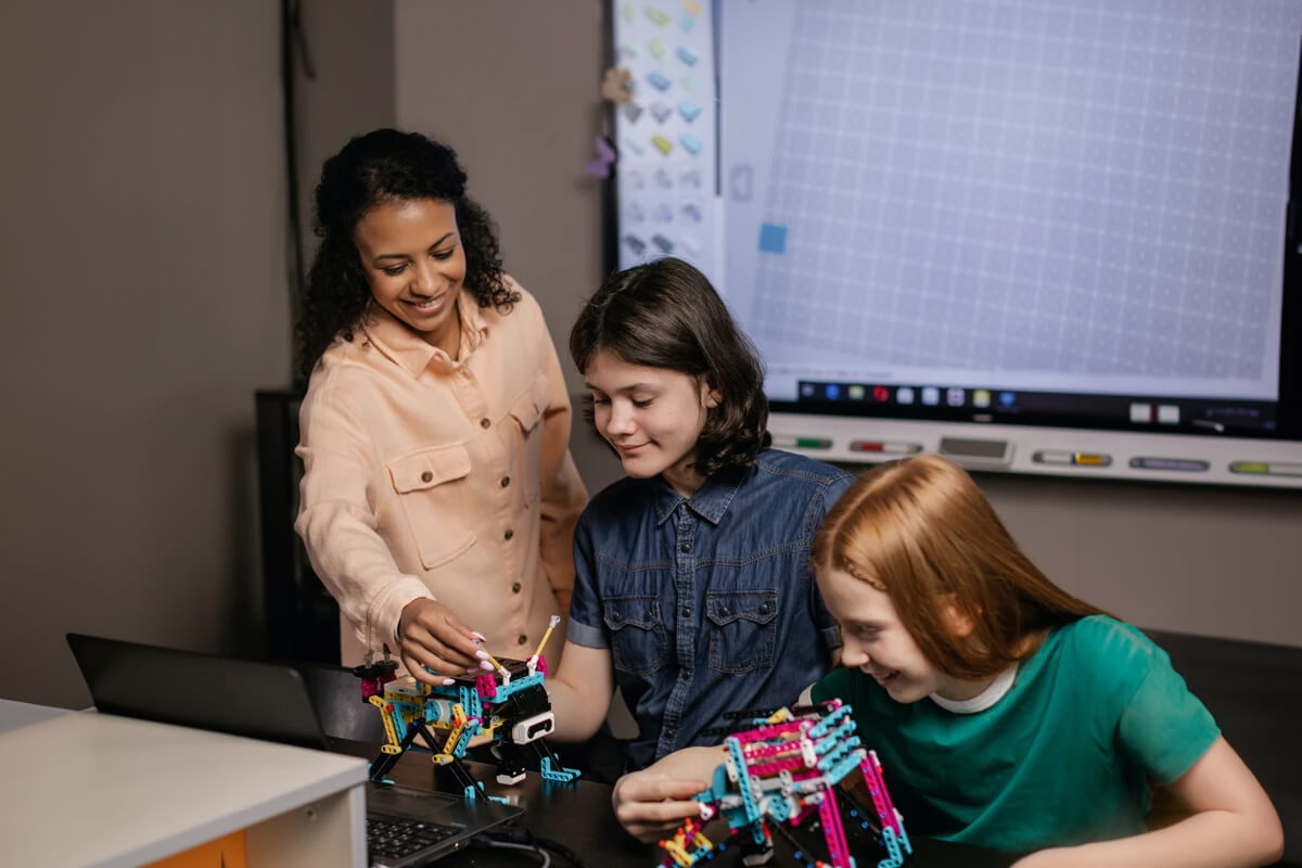 An ‘In2science’ mentor working together with two teenage girls to construct robots with LEGO Education SPIKE sets.