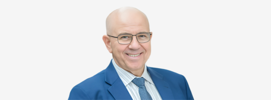 A well-dressed, dignified looking man in sharp reading glasses, smiling contently, Toyota Headquarters in Port Melbourne in the background.