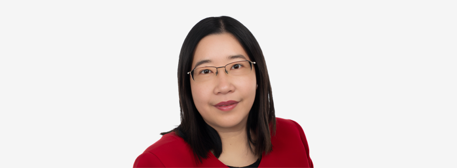 A woman with long straight dark brown hair, wearing slim, soft amber tinted glasses, smiling softly in front of a bright white backdrop