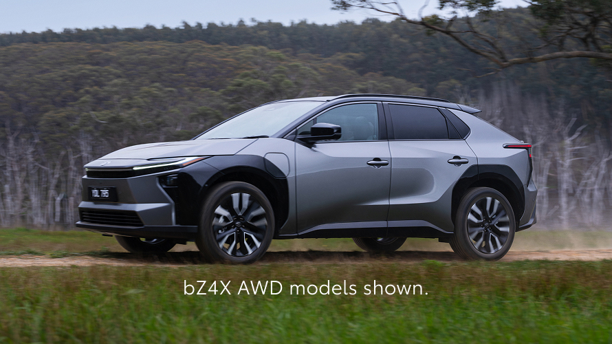 A bZ4X in Liquid Metal paint is displayed in a studio setting with soft lighting, highlighting its angular design and black roof accents. Text at the bottom reads, Pre-production models shown.