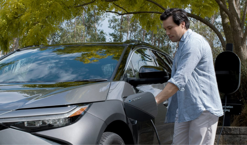 A man plugging in a grey Toyota bZ4X into a charging station outdoors.