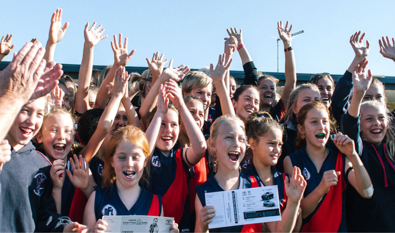 An Australian rules football team of young school girls, cheering in celebration.