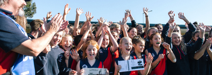 An Australian rules football team of young school girls, cheering in celebration.