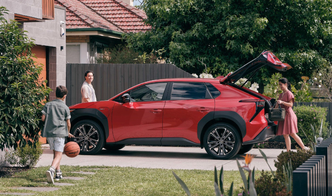 A family in front of their suburban home, preparing to get into their red Toyota bZ4X.