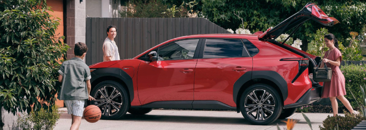 A family in front of their suburban home, preparing to get into their red Toyota bZ4X.