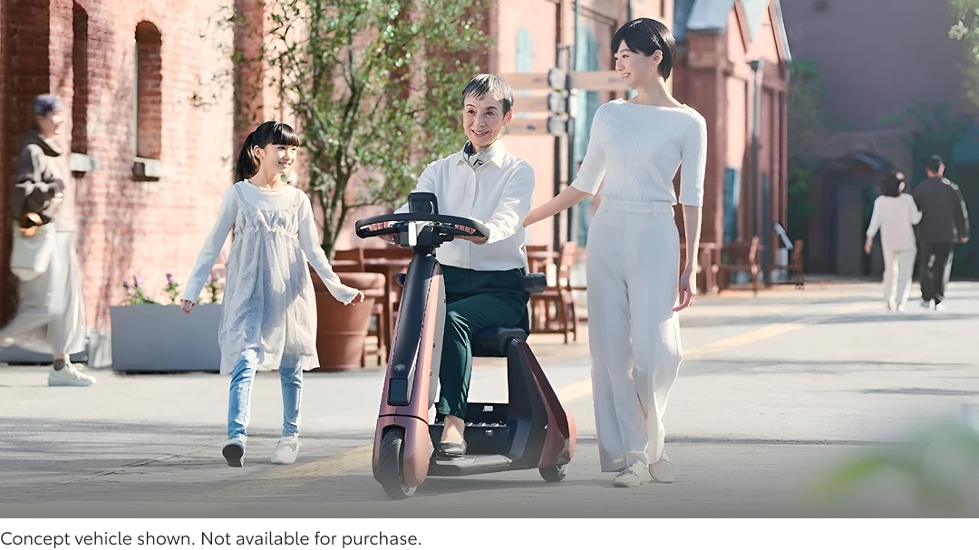 A mother, grandmother and daughter travelling down a suburban footpath together on a sunny day, the grandmother on a futuristic mobility scooter.