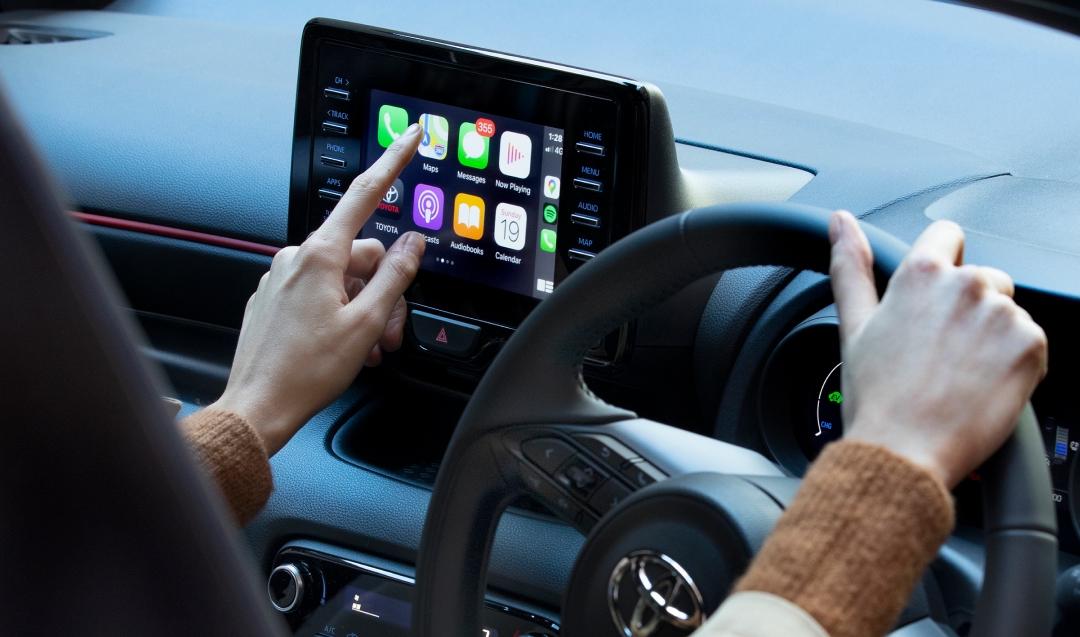 A person sitting in the driver's seat of a toyota using the multimedia touch screen, about to access the maps feature.