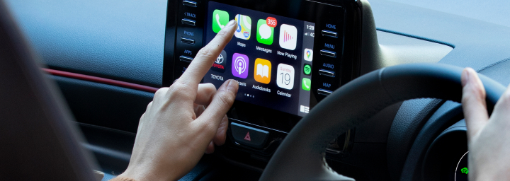 A person sitting in the driver's seat of a toyota using the multimedia touch screen, about to access the maps feature.