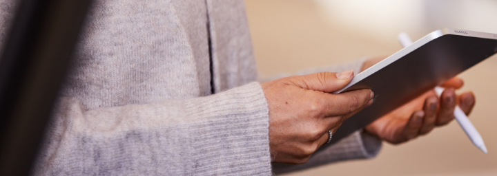 A woman stands next to a Toyota Dealer, holding a digital tablet and accompanying pen, the door of a blue Toyota ajar.