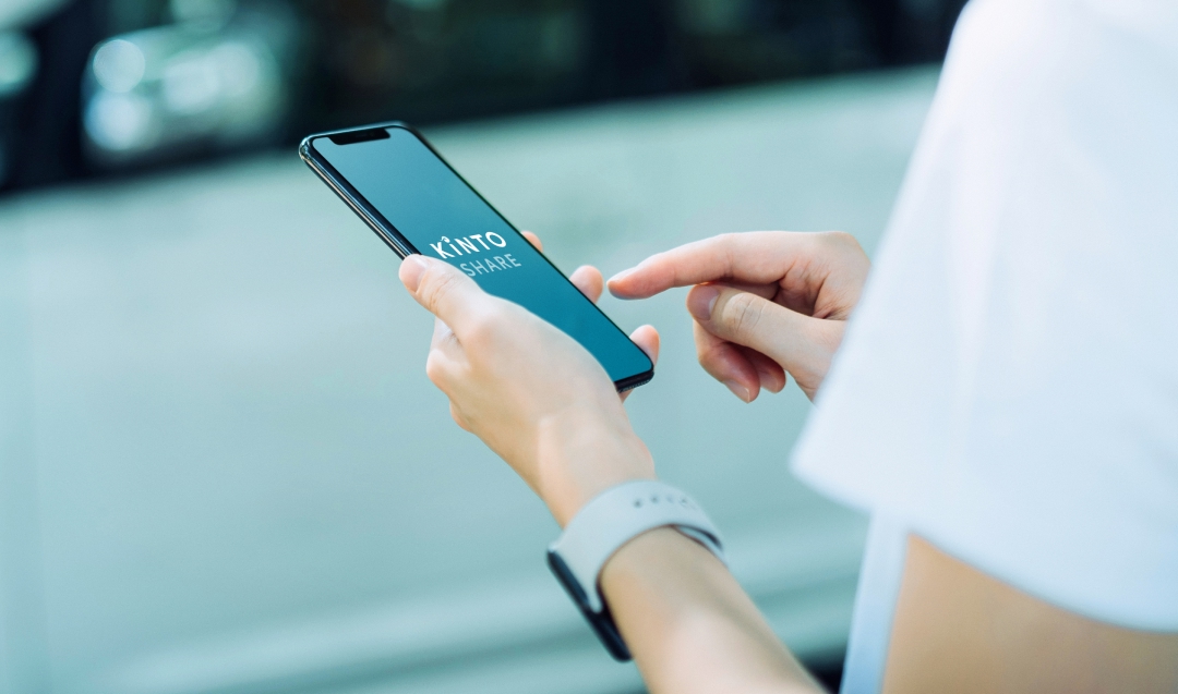 A person standing by the side of a road, accessing the Kinto app on their mobile device.