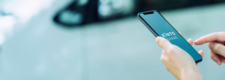 A person standing by the side of a road, accessing the Kinto app on their mobile device.