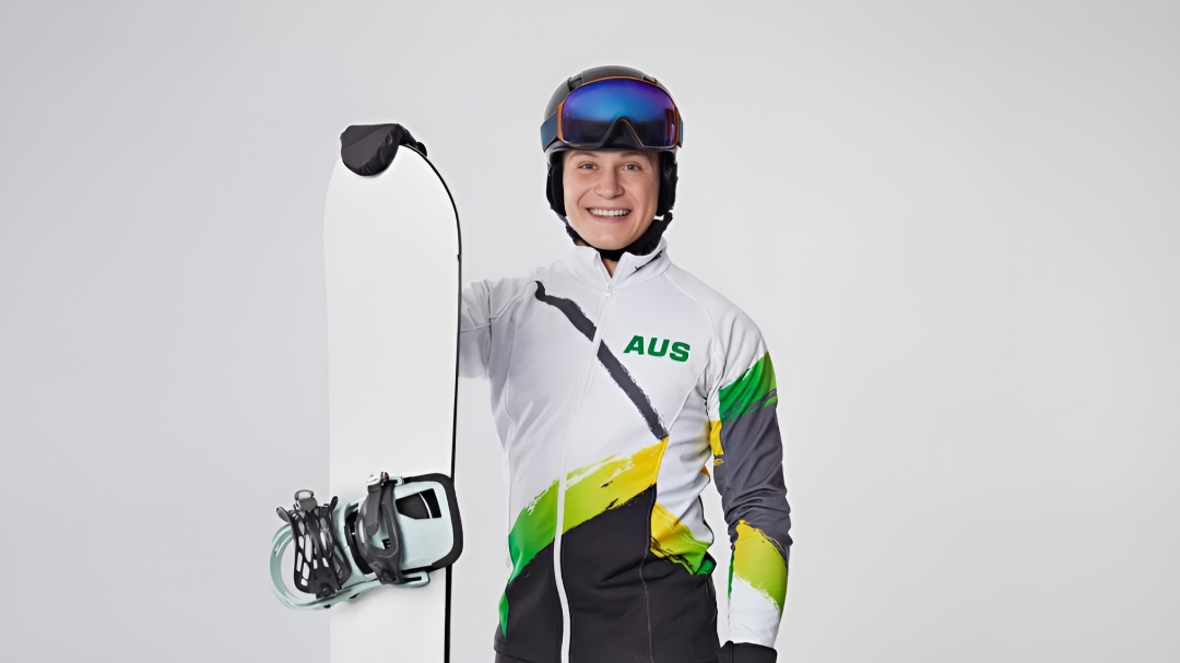 Australian Paralympian snowboarder Ben Tudhope stands proudly in snowboarding gear, his snowboard held up with his right hand.
