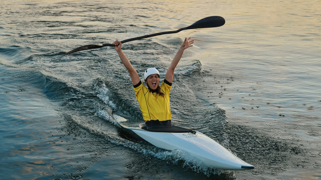 Australian Olympian canoeist Jess Fox, canoeing, raising her hands and paddle in the air in celebration.