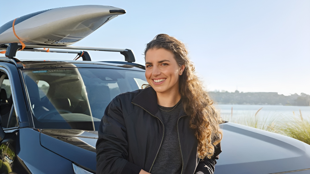 Australian Olympian canoeist Jess Fox smiling in the sun, leaning against her black RAV4, a canoe fastened to the top.