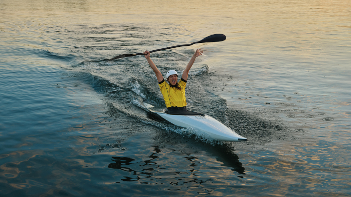 Australian Olympian canoeist Jess Fox, canoeing, raising her hands and paddle in the air in celebration.
