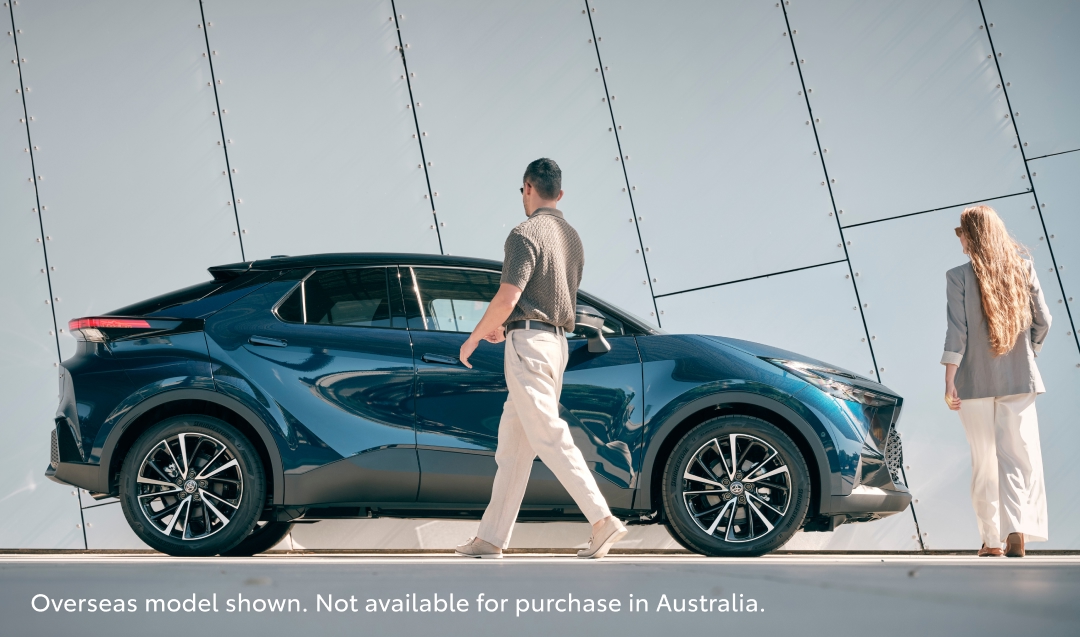 A man and a woman, both smartly dressed, approaching a shiny blue Toyota C-HR.
