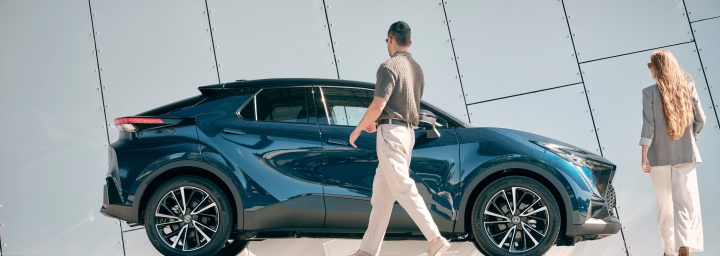 A man and a woman, both smartly dressed, approaching a shiny blue Toyota C-HR.