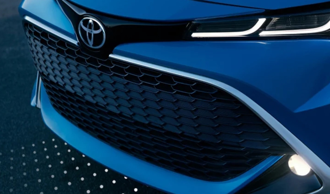 An artistically photographed front grille and left headlight of a blue 2024 Toyota Corolla in the ZR grade, headlights on, in a cool, moody atmosphere. 