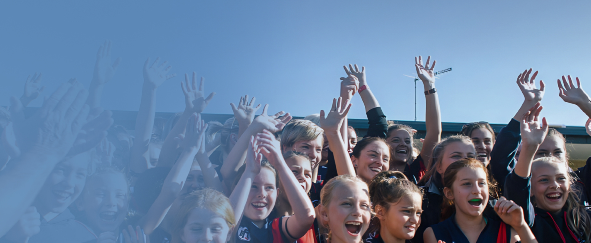 An Australian rules football team of young school girls, cheering in celebration.