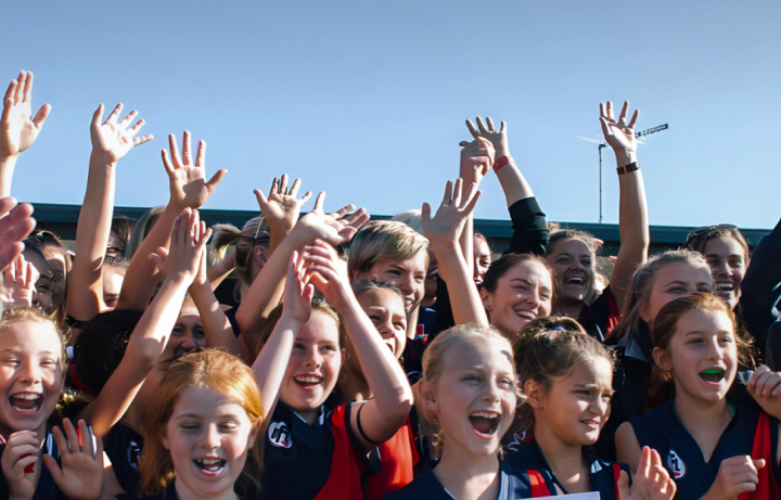 An Australian rules football team of young school girls, cheering in celebration.