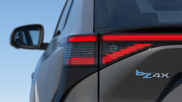 A rear view of the all-electric Toyota bZ4X in the liquid metal paint colour, with red tail lights and a bZ4X badge. 