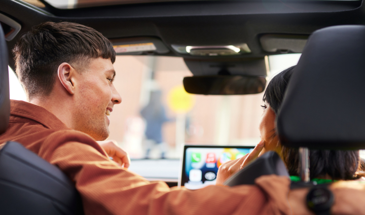 A young man and woman sit talking and smiling in the front seat of a Toyota passenger car.