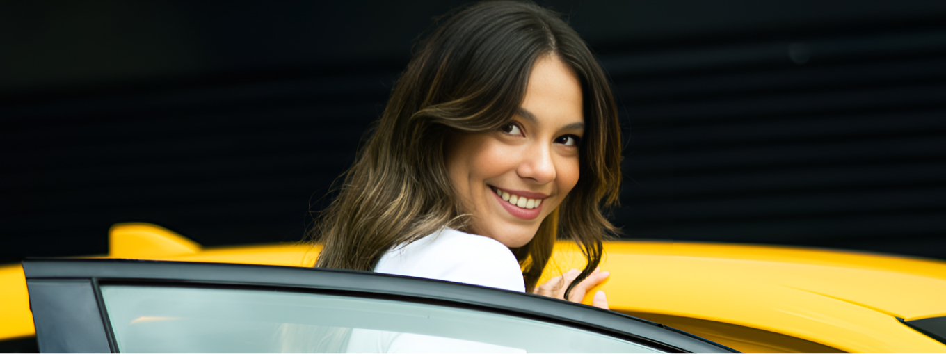 A woman entering a yellow vehicle, looking over her shoulder, smiling brightly.