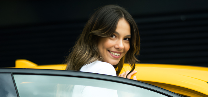 A woman entering a yellow vehicle, looking over her shoulder, smiling brightly.